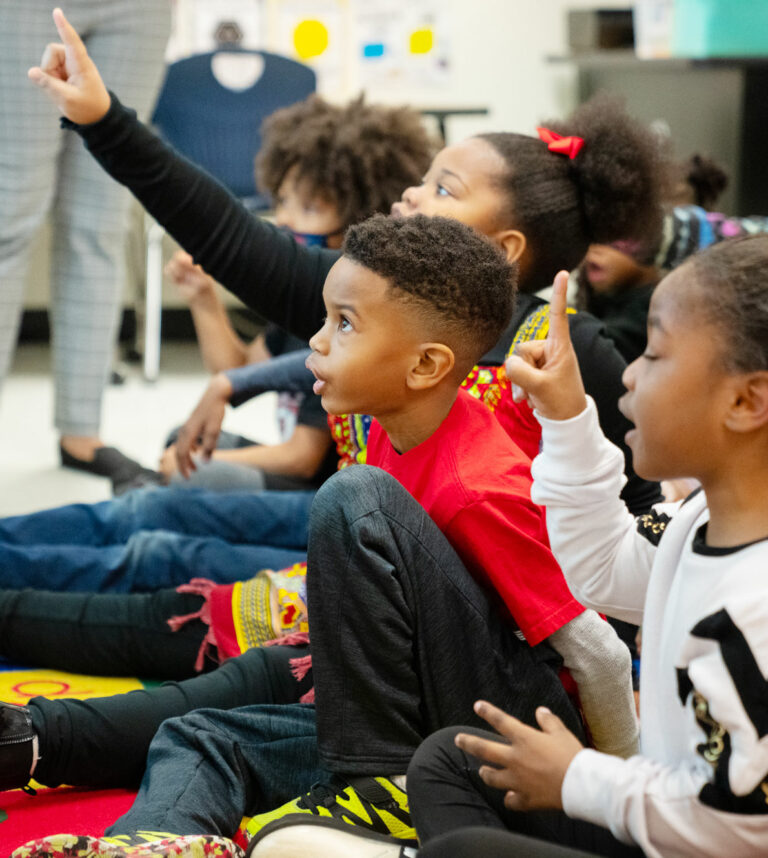 Energetic elementary school students raising hands during a phonics lesson