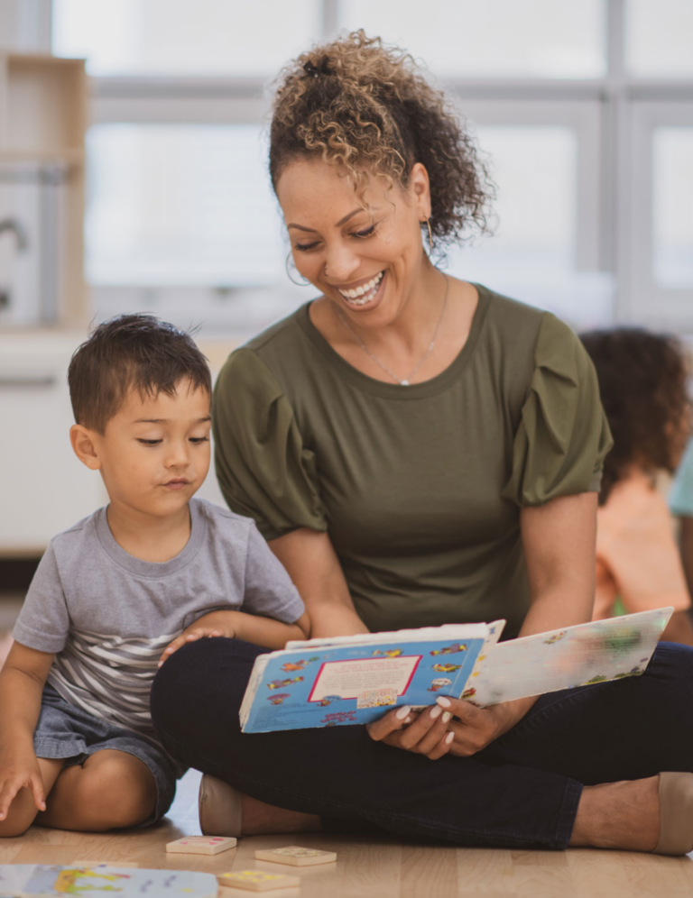 Adult and child reading a book together on the floor surrounded by toys